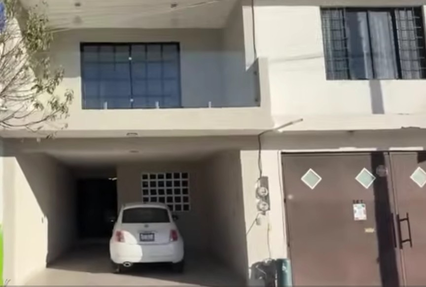 La vista exterior de la casa muestra un diseño sencillo en tonos claros, con un amplio garaje en la planta baja con espacio para su automóvil.